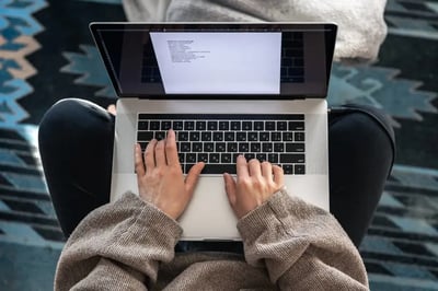 Woman typing on a laptop while sitting cross-legged, viewed from above.